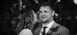 Braut flüstert Bräutigam ins Ohr – Schwarzweißporträt von einem Hochzeitspaar vor natürlichem Hintergrund