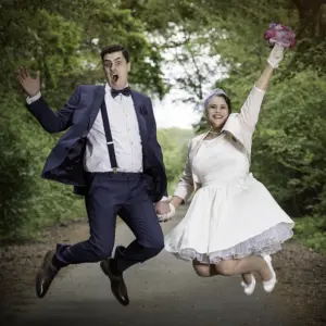 Hochzeitsfotograf Pfalz – Brautpaar springt im Vintage-Look vor grüner Kulisse